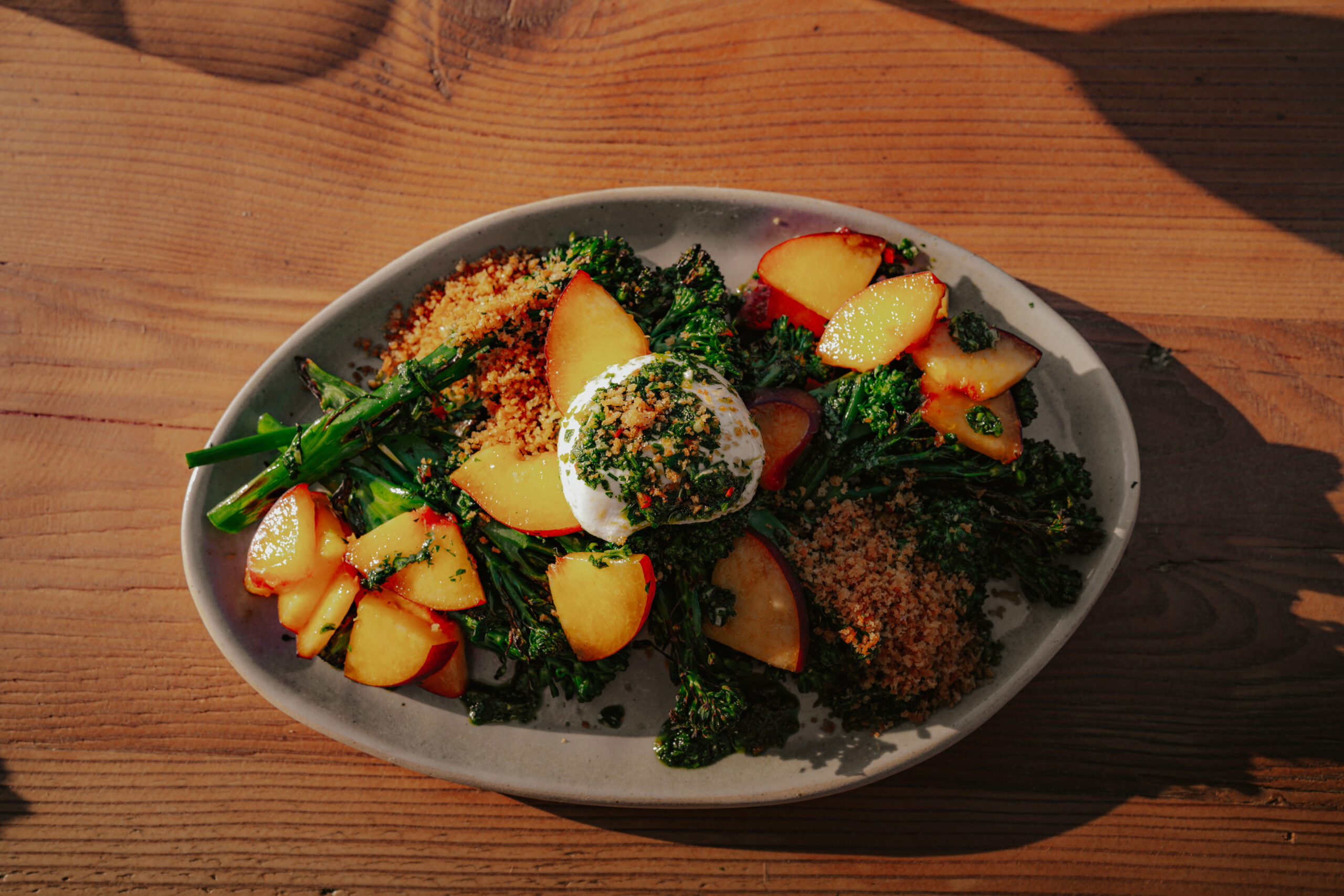 Roasted broccolini salad with sliced peaches, burrata cheese, and herbed breadcrumbs on a ceramic plate