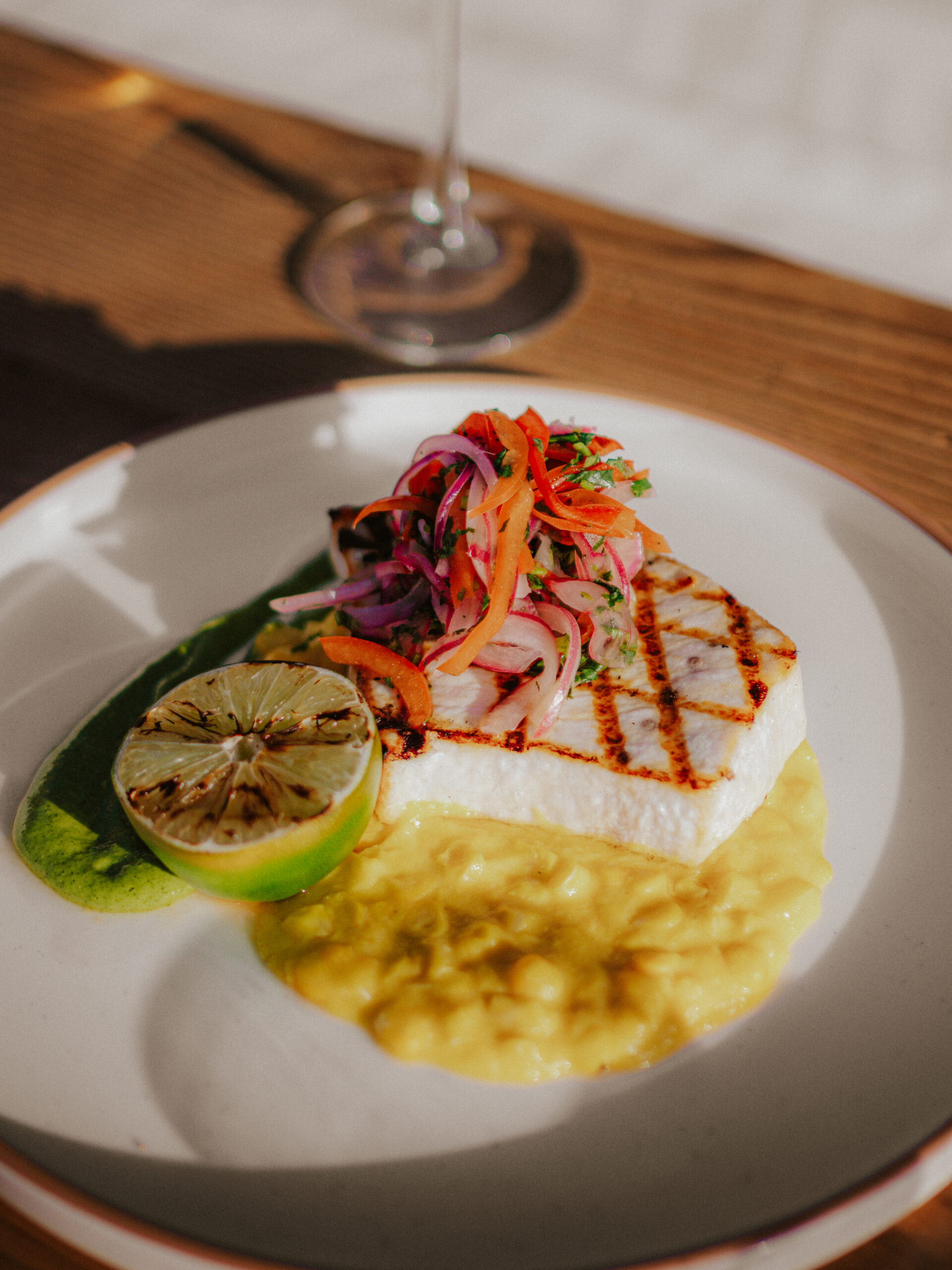 Grilled fish filet served over creamy puree with pickled vegetables and a charred lime garnish